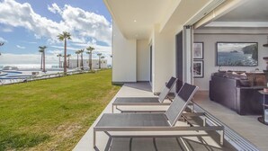 A modern outdoor seating area with lounge chairs and a pool, overlooking a beach with palm trees and a clear sky. - Phenomenal 3 Bedroom Condo Encantame Tower E 101 (Puerto Peñasco)