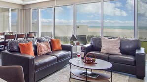 A modern living room with leather sofas, a coffee table, and large windows offering a view of the beach. - Phenomenal 3 Bedroom Condo Encantame Tower E 101 (Puerto Peñasco)