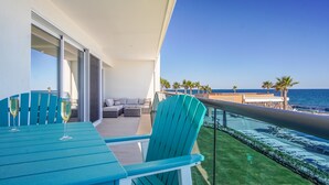 Ein Balkon mit Meerblick, eine Sitzecke mit einer Couch und Sesseln sowie ein Tisch mit zwei Weingläsern.