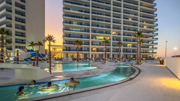 Ein Hotel mit mehreren Schwimmbecken, Palmen und einem großen Gebäude mit Balkonen.