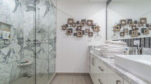 Ένα σύγχρονο μπάνιο με καμπίνα ντους από γυαλί, επένδυση τοίχου από μάρμαρο και κρεμαστή ράγα για πετσέτες.