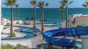 A resort pool area with a water slide, palm trees, and a view of the ocean.