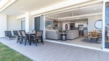 A modern open-plan living area with a dining area, kitchen, and a glass door leading to a patio.