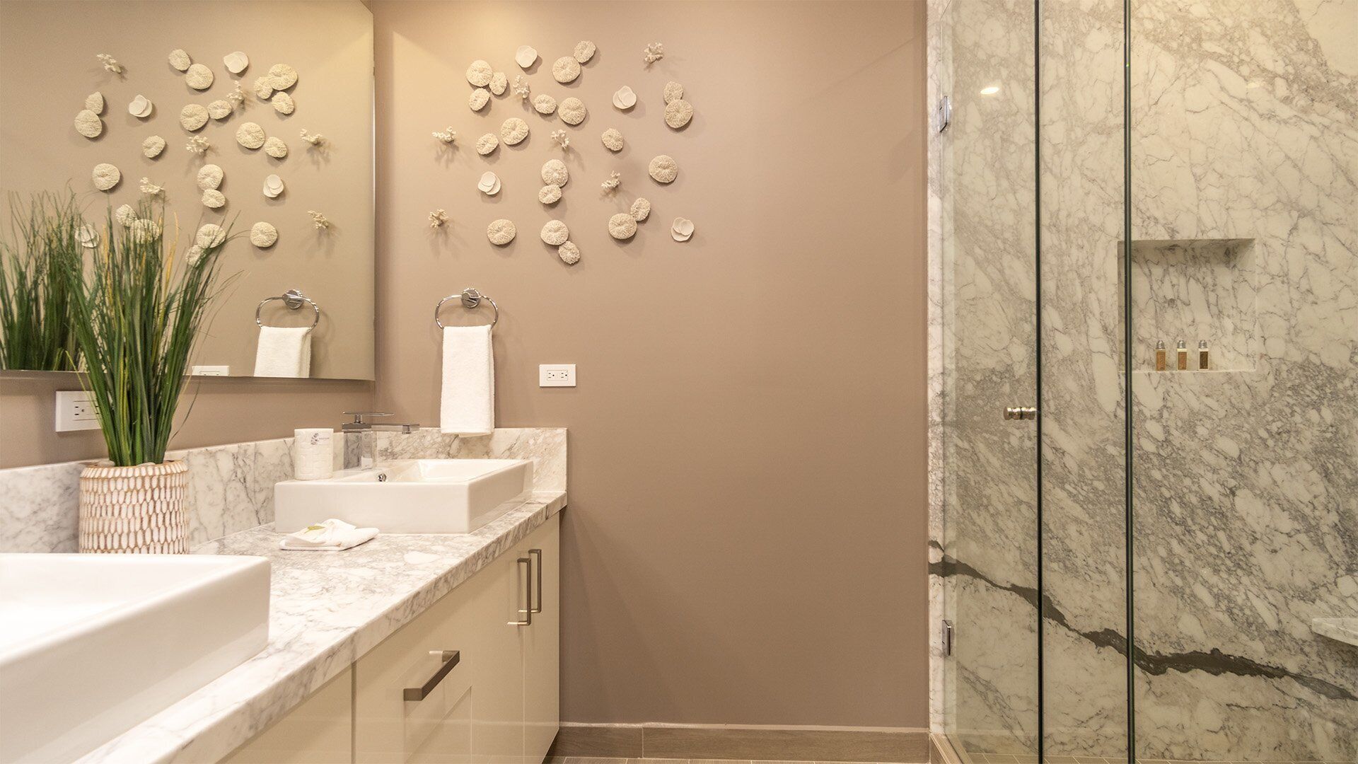 A modern bathroom with a marble shower, a large mirror, and decorative wall art.
