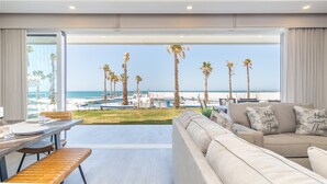A modern living room with a large window overlooking a beach and palm trees. - Encantame Towers Viento 105 (Puerto Peñasco)