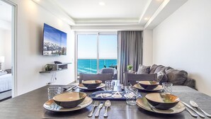 A dining area with a view of the sea, a TV mounted on the wall, and a sofa with cushions. - Panoramic Beach Front Condo Verano 1703 (Puerto Peñasco)