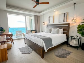A modern bedroom with a large bed, a balcony with a view of the sea, a ceiling fan, and a small table with chairs. - Stunning 2 Bedroom Corner Beach Front Condominium Encantame C-1105 (Puerto Peñasco)