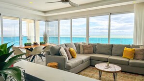 A spacious living area with a large sofa, a dining table, and a view of the ocean. - Stunning 2 Bedroom Corner Beach Front Condominium Encantame C-1105 (Puerto Peñasco)