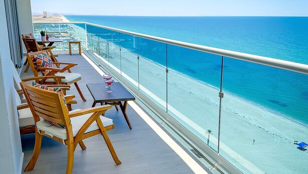 A balcony with wooden furniture, a table, and a view of the beach and ocean. - Stunning 2 Bedroom Corner Beach Front Condominium Encantame C-1105 (Puerto Peñasco)