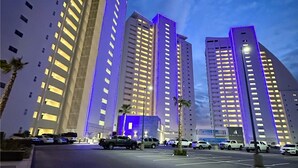 A modern high-rise building with multiple floors, featuring a prominent vertical light strip on the facade. - Stunning 2 Bedroom Corner Beach Front Condominium Encantame C-1105 (Puerto Peñasco)