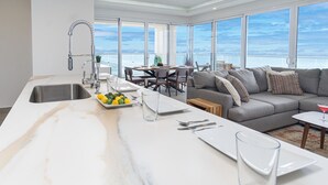 A modern kitchen with a marble countertop, a dining area with a gray sofa, and large windows overlooking the sea. - Stunning 2 Bedroom Corner Beach Front Condominium Encantame C-1105 (Puerto Peñasco)