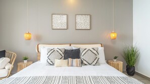 Een keurig opgemaakt slaapkamer met een groot bed, twee wandlampen en twee kunstwerken in lijsten.