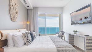 Ein modernes Hotelzimmer mit einem großen Bett, einem Balkon mit Meerblick, einer Sitzecke und einem Bild an der Wand.