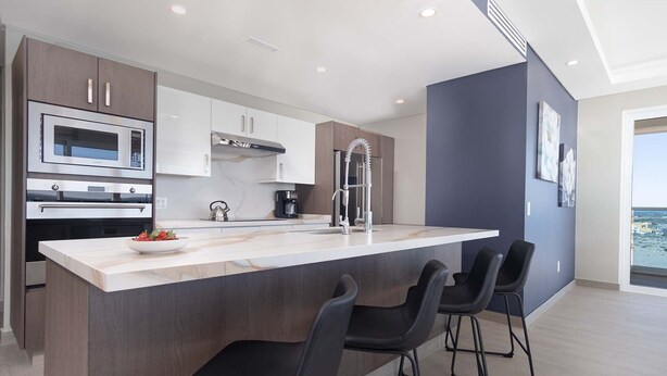 A modern kitchen with a central island, bar stools, and a view of the sea. - Splash in New Lazy River/stay in Modern Luxury Encantame C-705 (Puerto Peñasco)