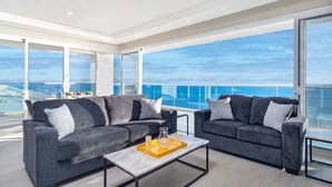 Ein modernes Wohnzimmer mit zwei grauen Sofas, einem Couchtisch und Blick auf den Ozean.