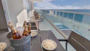 Ein Balkon mit Tisch, gedeckt für eine Mahlzeit, inklusive einem Eimer mit Bierflaschen und Schüsseln mit Popcorn, mit Blick auf einen Strand und den Ozean.