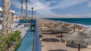 A beach resort with a pool, sun loungers, thatched umbrellas, and palm trees. - Waterfront Getaway 2 Bedroom Condo W1102 (Puerto Peñasco)