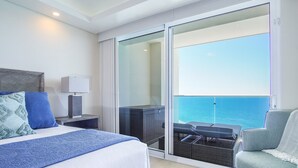 Une chambre d’hôtel comprenant un lit, une table de chevet, une lampe, une chaise et un balcon avec vue sur la mer.