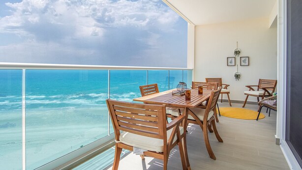 Un balcon avec une table et des chaises en bois, donnant sur une mer et un ciel d’un bleu limpide.