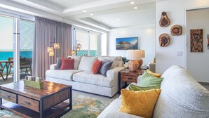Un salon spacieux avec un grand canapé, une table basse et une vue sur l’océan grâce à de grandes fenêtres.