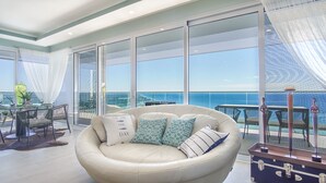 Un ampio balcone con vista sull'oceano, un divano in pelle rotondo con cuscini decorati e un'area pranzo con tavolo e sedie.