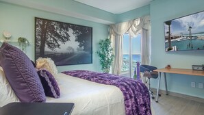 Una camera da letto con un letto, una scrivania, una sedia, una finestra vista spiaggia e un quadro appeso al muro.