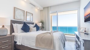 Un dormitorio moderno con una cama grande, una mesita de noche, un aparador y vistas al océano.