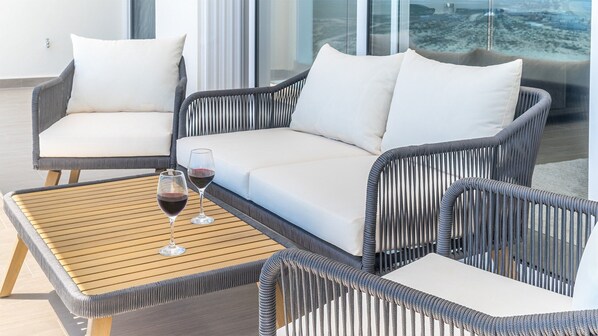 A modern outdoor seating area with wicker furniture and white cushions, featuring a wooden table with two wine glasses.