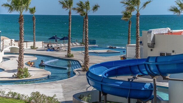 Un área de piscina en un resort con múltiples toboganes de agua, palmeras y vistas al océano.