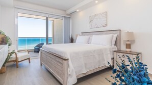 A bedroom with a large bed, a nightstand, a chair, and a view of the ocean through a sliding door. - Beach Getaway 2 Bedroom Condo W802 (Puerto Peñasco)