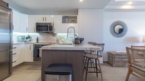 Una cocina moderna con electrodomésticos de acero inoxidable, una isla central con taburetes y un comedor con sillas de mimbre.