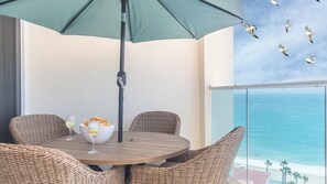 Et spiseområde i et hjørne med fletstole, et rundt bord og en grøn parasol.