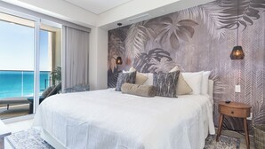 Un dormitorio con una cama grande, vista al océano y un papel tapiz con motivos de hojas tropicales.