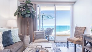 Una sala de estar moderna con vista al océano, un balcón con mobiliario exterior y una planta grande.