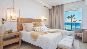 Ein modernes Schlafzimmer mit einem großen Bett, Nachttischen, einer Bank und Meerblick.