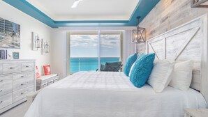 A bedroom with a large bed, a view of the ocean, and a wooden headboard.