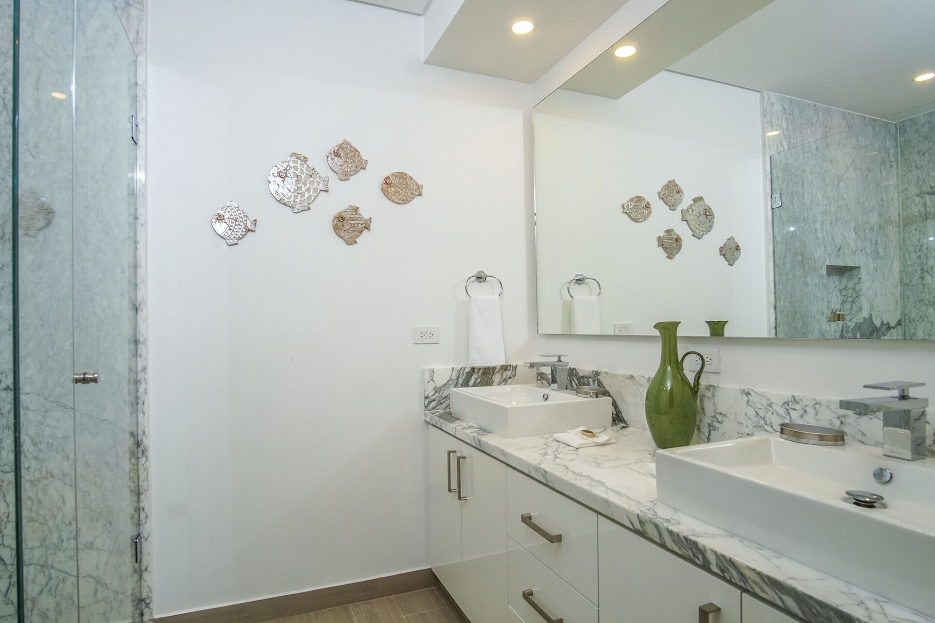 Une salle de bain moderne avec deux lavabos, un grand miroir et des décorations murales représentant des poissons.