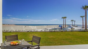 A patio with a table set for two, overlooking a pool area with palm trees and a view of the beach. - Spectacular 2 Bedroom Condominium Encantame E102 (Puerto Peñasco)