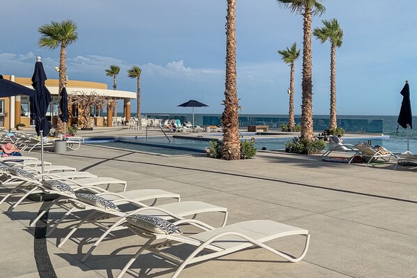 A poolside area with lounge chairs, palm trees, and a view of the ocean. - Family Paradise Splash in The New Lazy River and Sleep In Luxury Encantame Towers C 1701 (Puerto Peñasco)