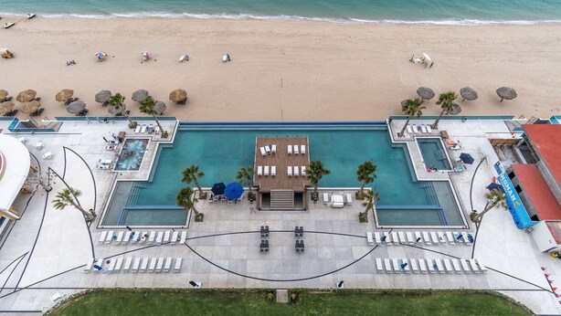 An aerial view of a resort with a central pool, multiple lounge areas, and a beach.