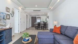 A modern living room with a grey sofa, a coffee table with decorative items, and a dining area with chairs and a kitchen counter.