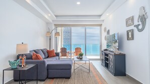 A modern living room with a grey sectional sofa, a small side table, a floor lamp, and a view of the ocean through large windows.