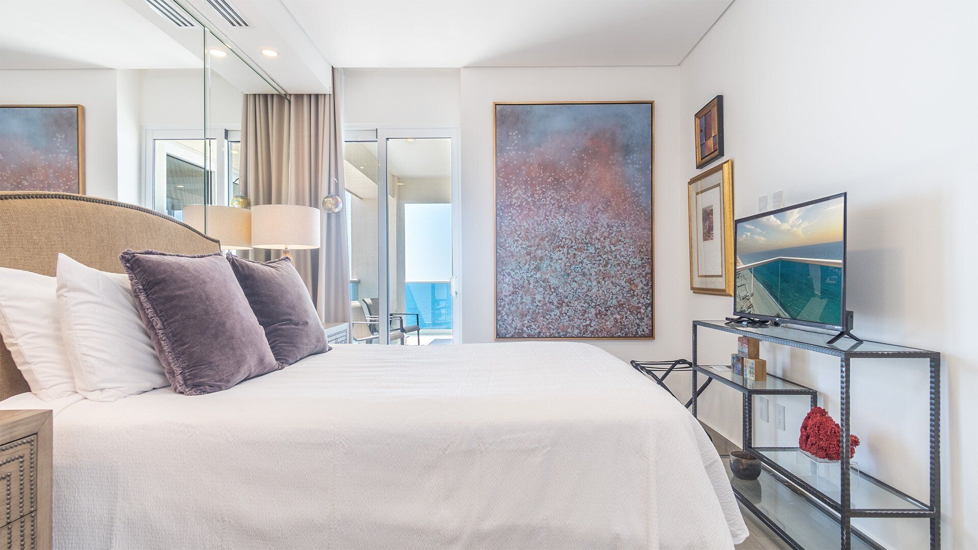 A hotel room with a large bed, a TV, and artwork on the walls.