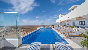 A rooftop infinity pool with lounge chairs, a glass balustrade, and a view of the desert landscape. - Encantame Towers Velero 2105 (Puerto Peñasco)