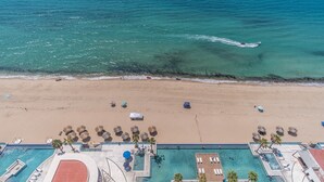An aerial view of a beach with a swimming pool area, including lounge chairs and umbrellas. - Encantame Towers Velero 2105 (Puerto Peñasco)