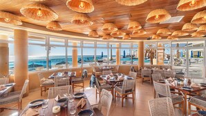 A restaurant with wicker furniture, large windows, and a view of the ocean. - Encantame Towers Velero 2105 (Puerto Peñasco)