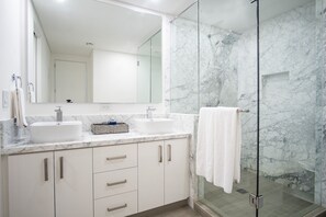 Ein modernes Badezimmer mit zwei Waschbecken, einem großen Spiegel und einer Duschkabine aus Glas.