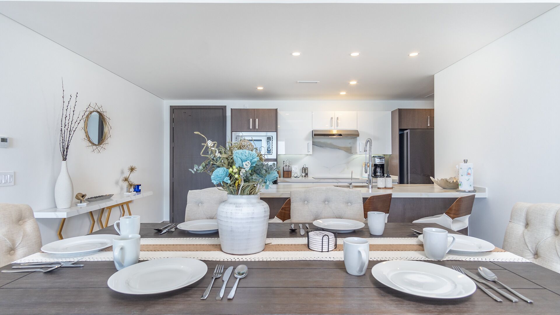 A modern dining area with a central island, white and grey furniture, and a vase with flowers.