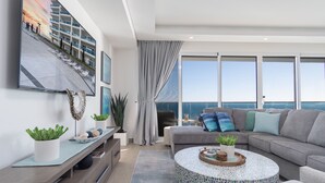 A modern living room with a large window, a grey sofa, a round coffee table, and a TV mounted on the wall. - Impressive & Beautiful 3 Bedroom end Unit Ocean Front Encantame C-1901 (Puerto Peñasco)