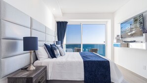 A modern bedroom with a large bed, a nightstand, a TV, and a balcony with a view of the sea. - Impressive & Beautiful 3 Bedroom end Unit Ocean Front Encantame C-1901 (Puerto Peñasco)